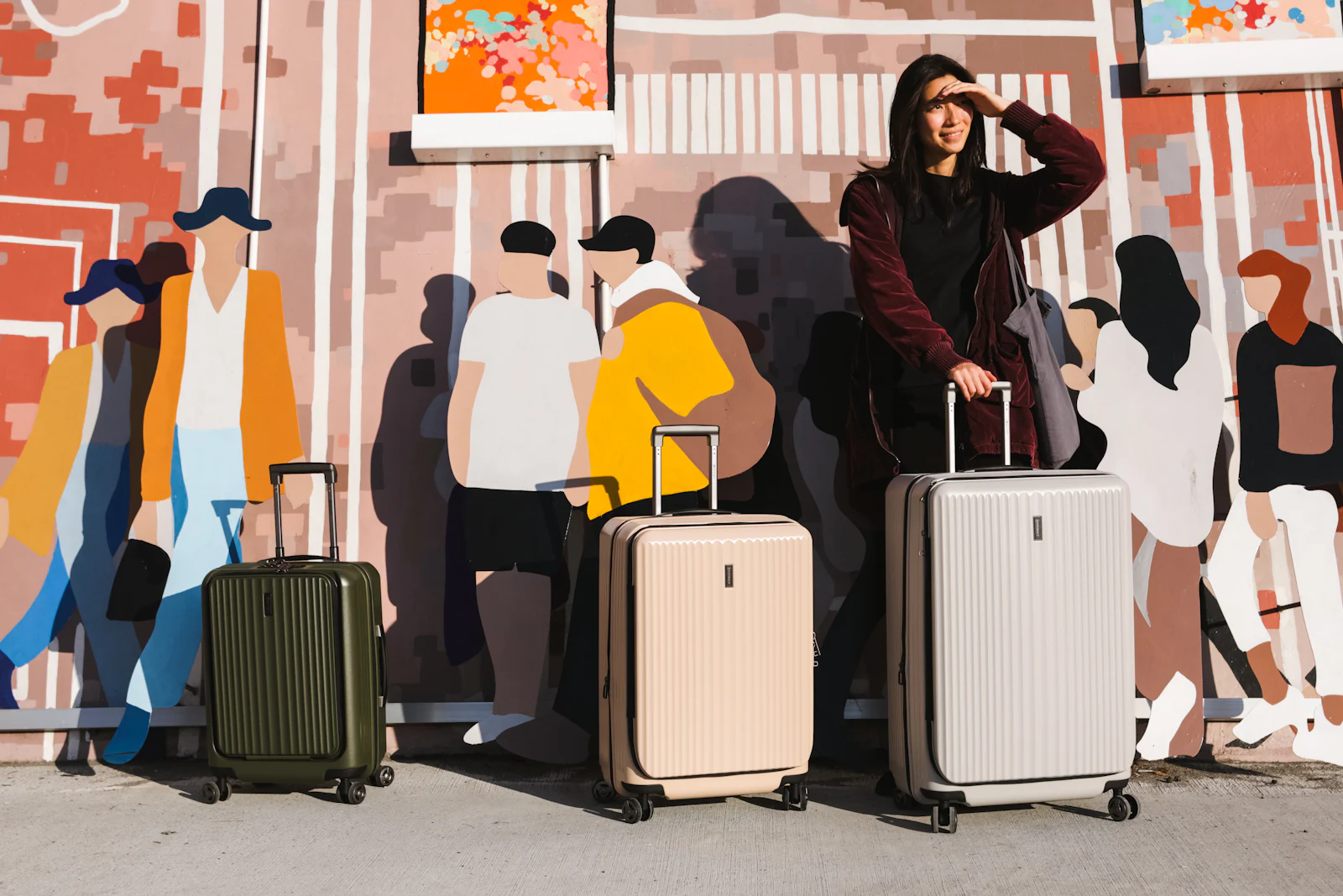 A traveller standing next to two suitcases in front of a painted city mural
