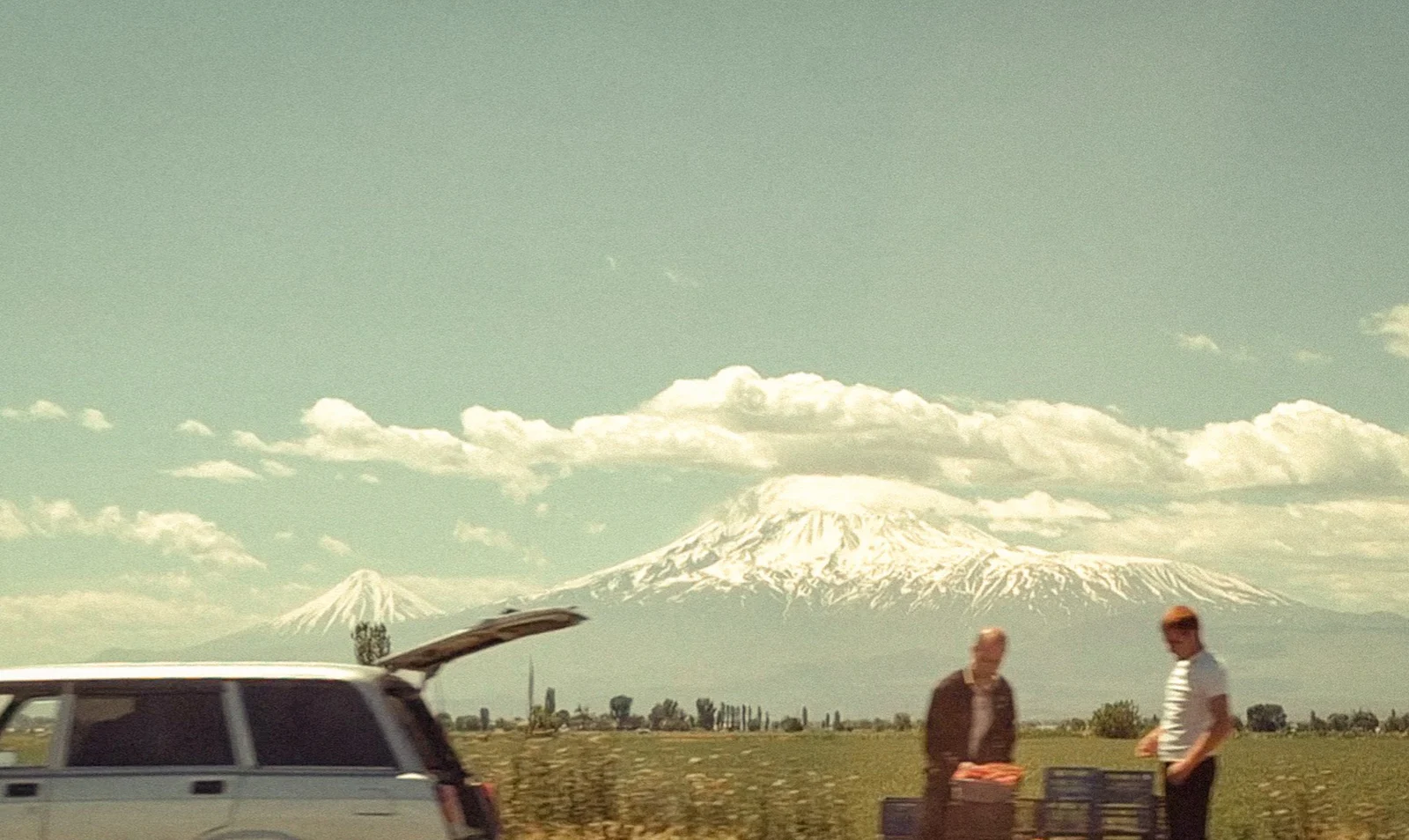 Two travellers unloading luggage from a car with a snow-capped mountain behind them