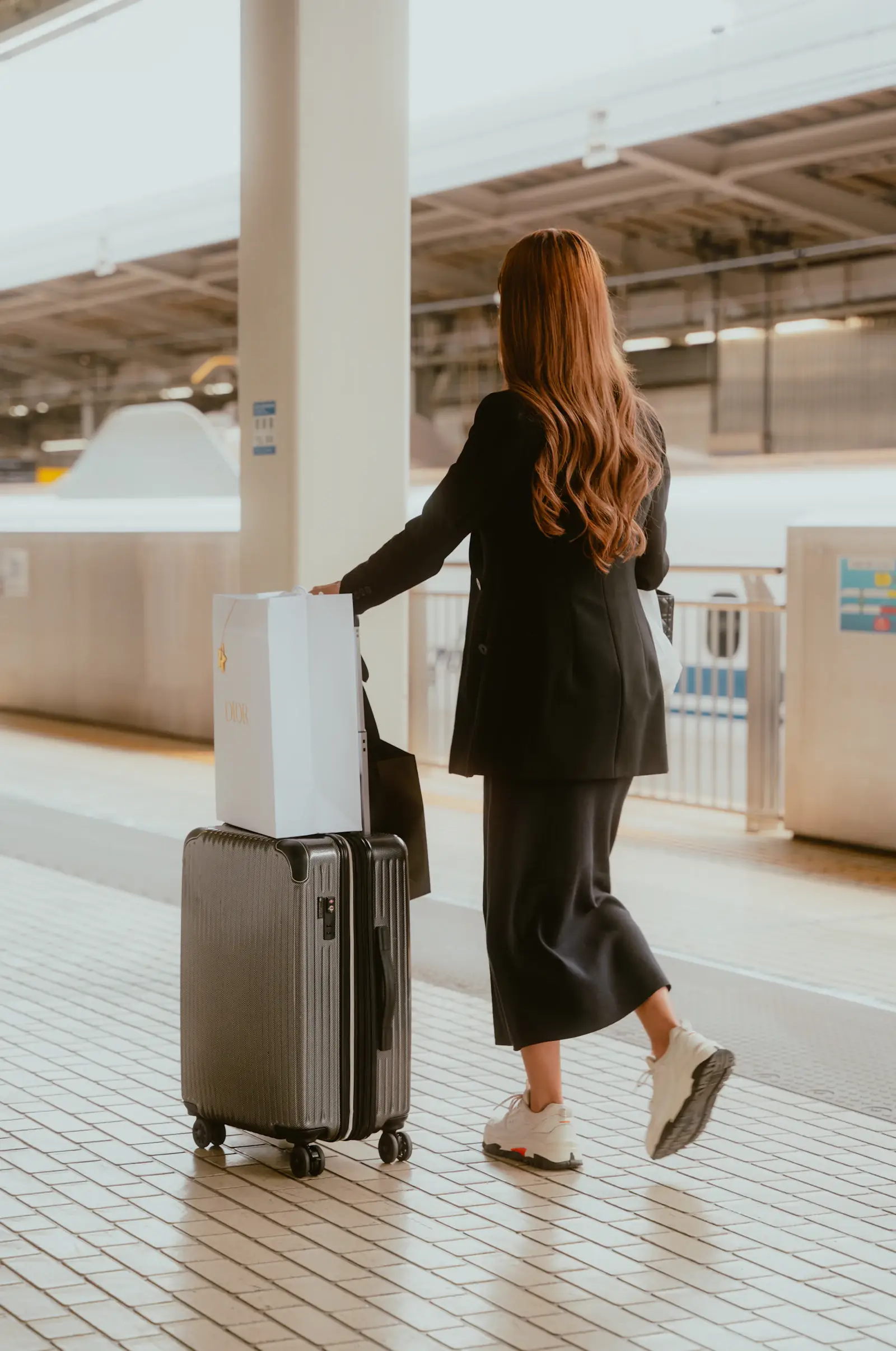 A traveller with a rolling suitcase waiting on a train station platform